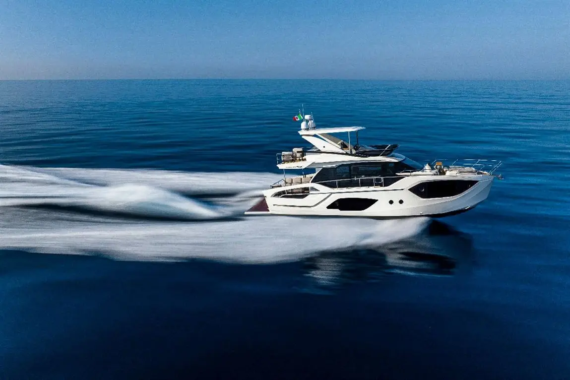 Luxury yacht cruising on calm blue waters, leaving a smooth wake; Italian flag visible on the vessel.